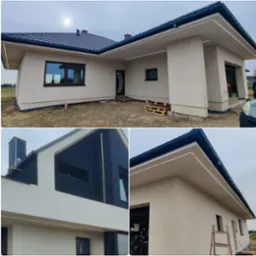 Nowoczesny dom jednorodzinny z zamontowanym oświetleniem LED na zewnątrz, widoczne detale elewacji i czarne orynnowanie, palety drewniane przed wejściem.