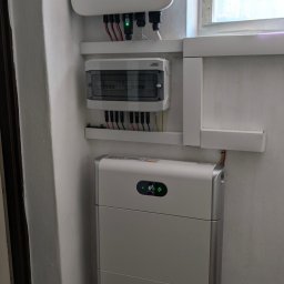 ELEQTRON - Biały falownik Huawei z podłączonymi kablami, skrzynka rozdzielcza i akumulator energii w pomieszczeniu z oknem.