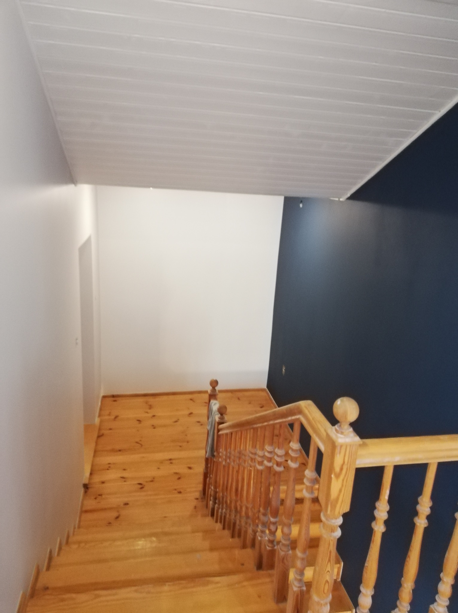 Schody drewniane z balustradą, ściany pomalowane na biało i granatowo, sufit z paneli PCV.