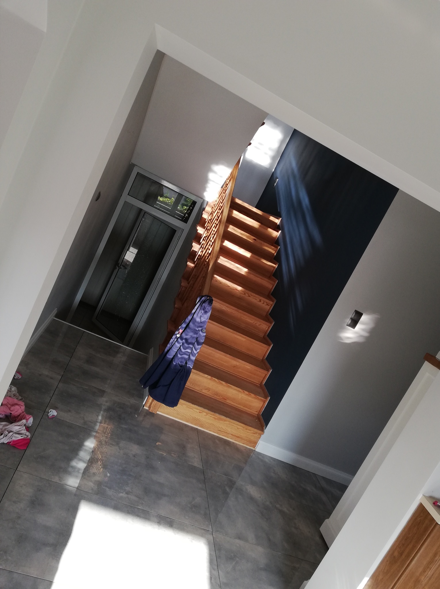 Widok z góry na odnowione wnętrze domu z drewnianymi schodami, szarą podłogą z płytek i ścianami pomalowanymi na biało i granatowo, z elementami garderoby na podłodze.