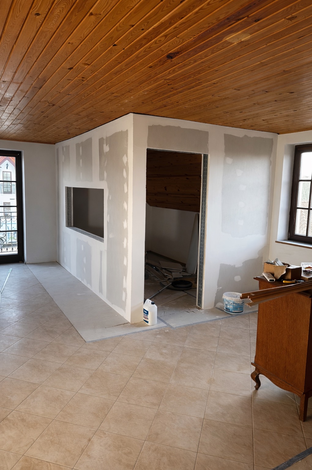 Wnętrze w trakcie prac wykończeniowych: ściany z płyt gipsowo-kartonowych, częściowo wyszpachlowane, drewniany sufit, widoczne narzędzia i materiały budowlane.