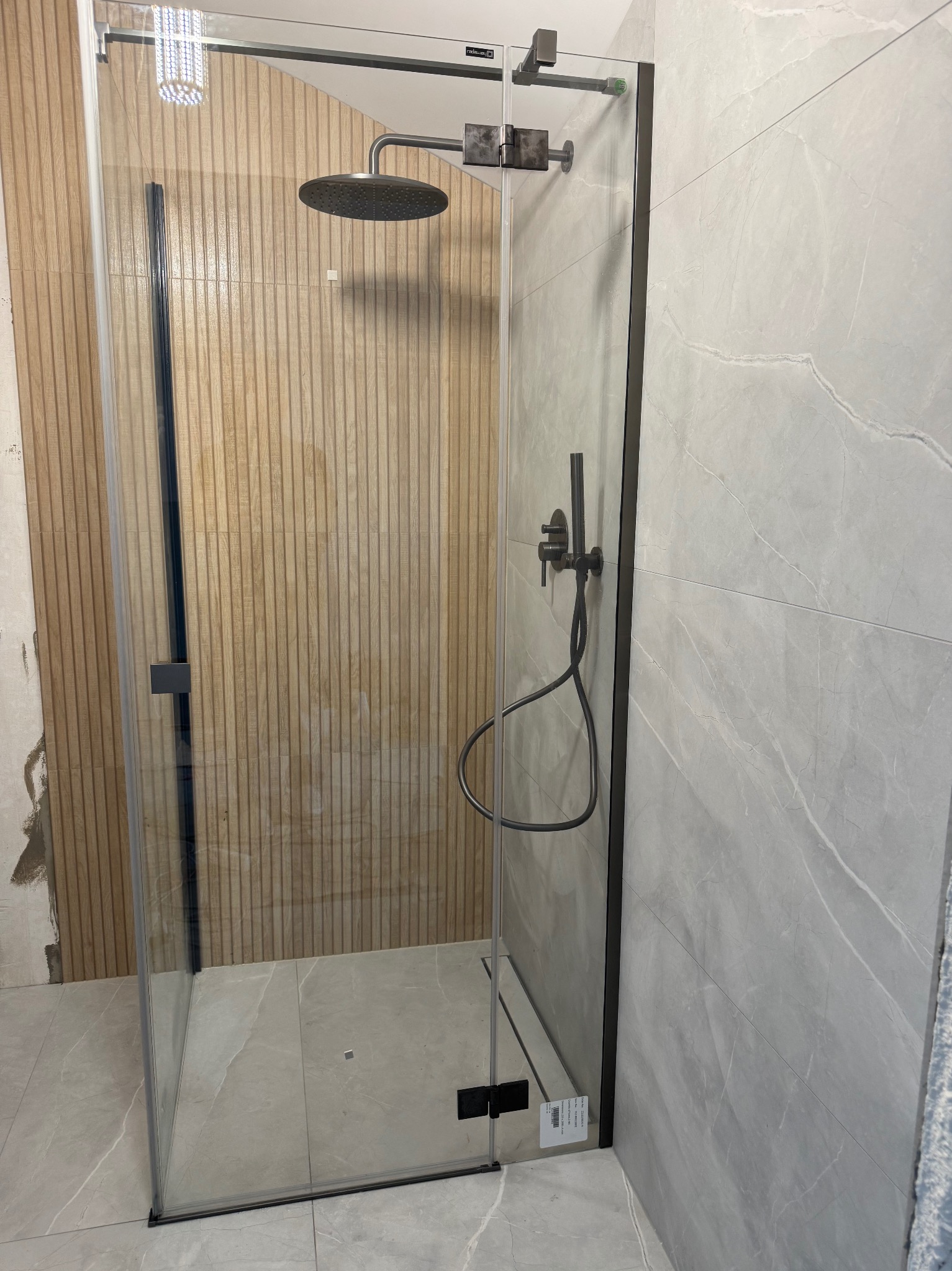 Nowoczesna kabina prysznicowa z czarnymi profilami i deszczownicą, wykończona płytkami imitującymi drewno i marmur, widoczna na tle częściowo wykończonej łazienki.