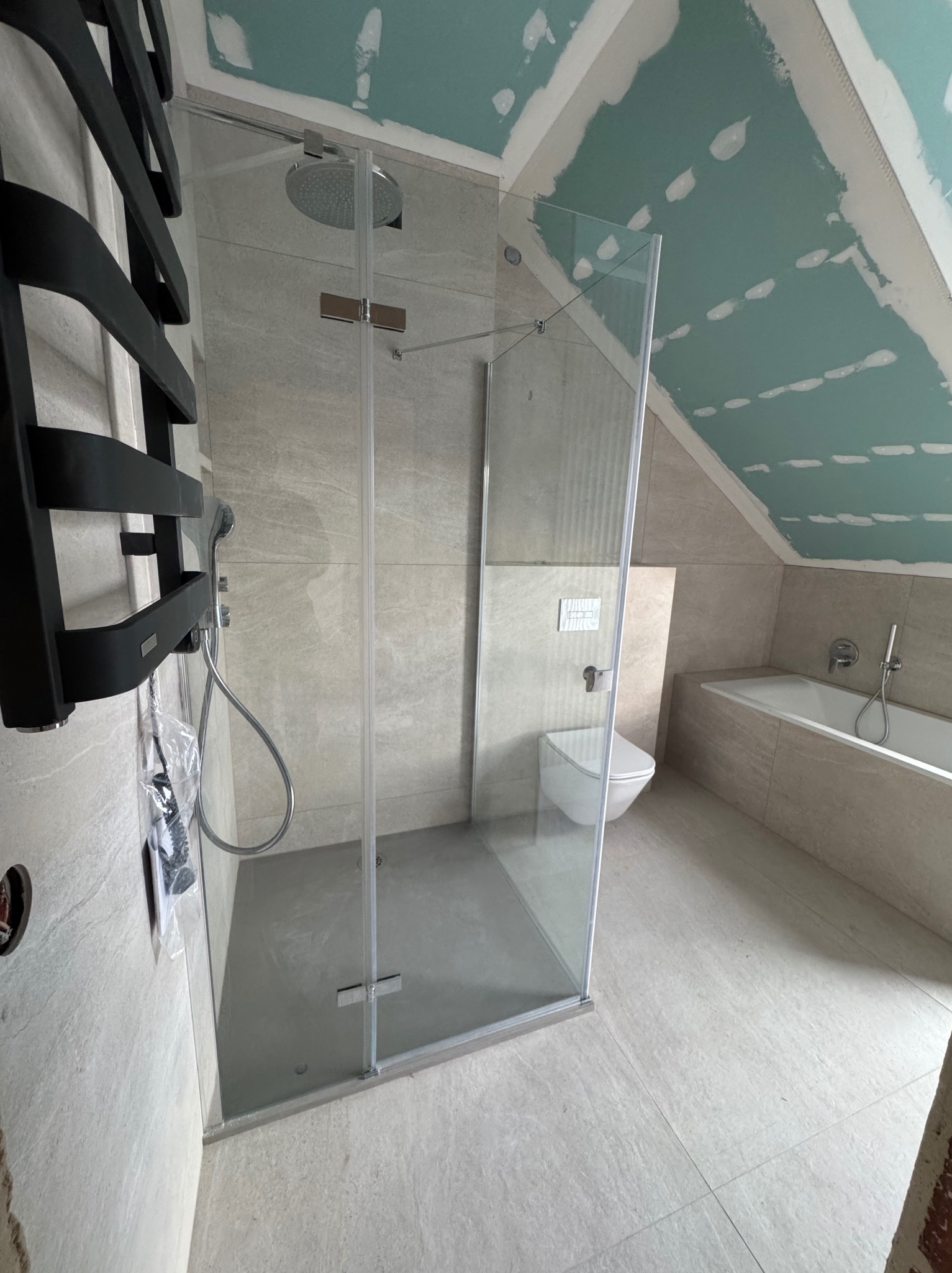 Nowoczesna łazienka w skandynawskim stylu: kabina prysznicowa ze szklanymi drzwiami, grzejnik drabinkowy i wanna w zabudowie, w jasnych płytkach imitujących kamień.