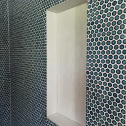 Niebiesko-zielona mozaika z okrągłych płytek w łazience z wnęką wyłożoną jasnymi płytkami.