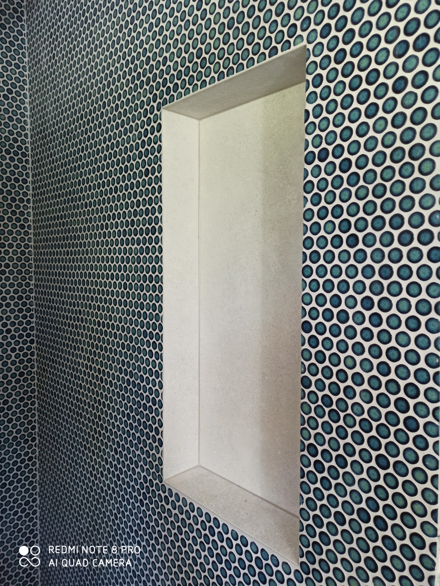 Niebiesko-zielona mozaika z okrągłych płytek w łazience z wnęką wyłożoną jasnymi płytkami.