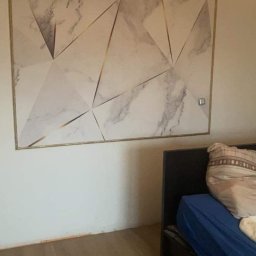 GrimzSa Remonty i wykończenia mieszkań - Geometryczny wzór marmuru z złotymi liniami na ścianie w sypialni, widoczny fragment łóżka z niebieską pościelą i poduszką.
