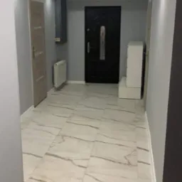 Wykończony korytarz w mieszkaniu z biało-szarą marmurową podłogą, szarymi ścianami, czarnymi drzwiami wejściowymi i białymi meblami.