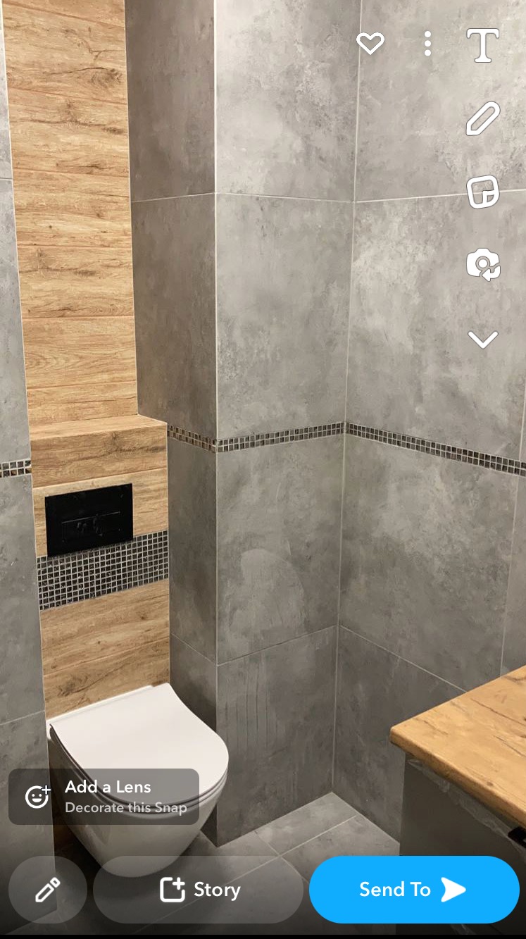 Nowoczesna łazienka z szarymi płytkami imitującymi beton, drewnianymi akcentami i podwieszaną toaletą.