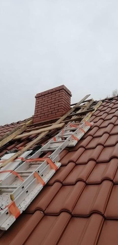 Czerwona dachówka ceramiczna z kominem z cegły podczas remontu, drabina oparta o dach.