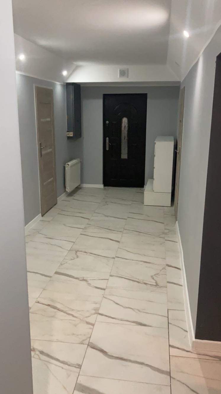 Wykończony korytarz w mieszkaniu z biało-szarą marmurową podłogą, szarymi ścianami, czarnymi drzwiami wejściowymi i białymi meblami.