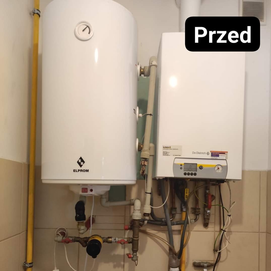 Biały, wiszący bojler Elprom i piec gazowy De Dietrich przed montażem. Widoczne rury, zawory oraz fragment żółtej instalacji gazowej.