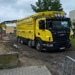 Przedsiębiorstwo Usługowe Tech-Sam - Żółta ciężarówka z ramieniem ssącym, zaparkowana na błotnistym terenie w Ślesinie, prawdopodobnie podczas prac kanalizacyjnych.