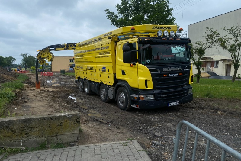 Żółta ciężarówka z ramieniem ssącym, zaparkowana na błotnistym terenie w Ślesinie, prawdopodobnie podczas prac kanalizacyjnych.