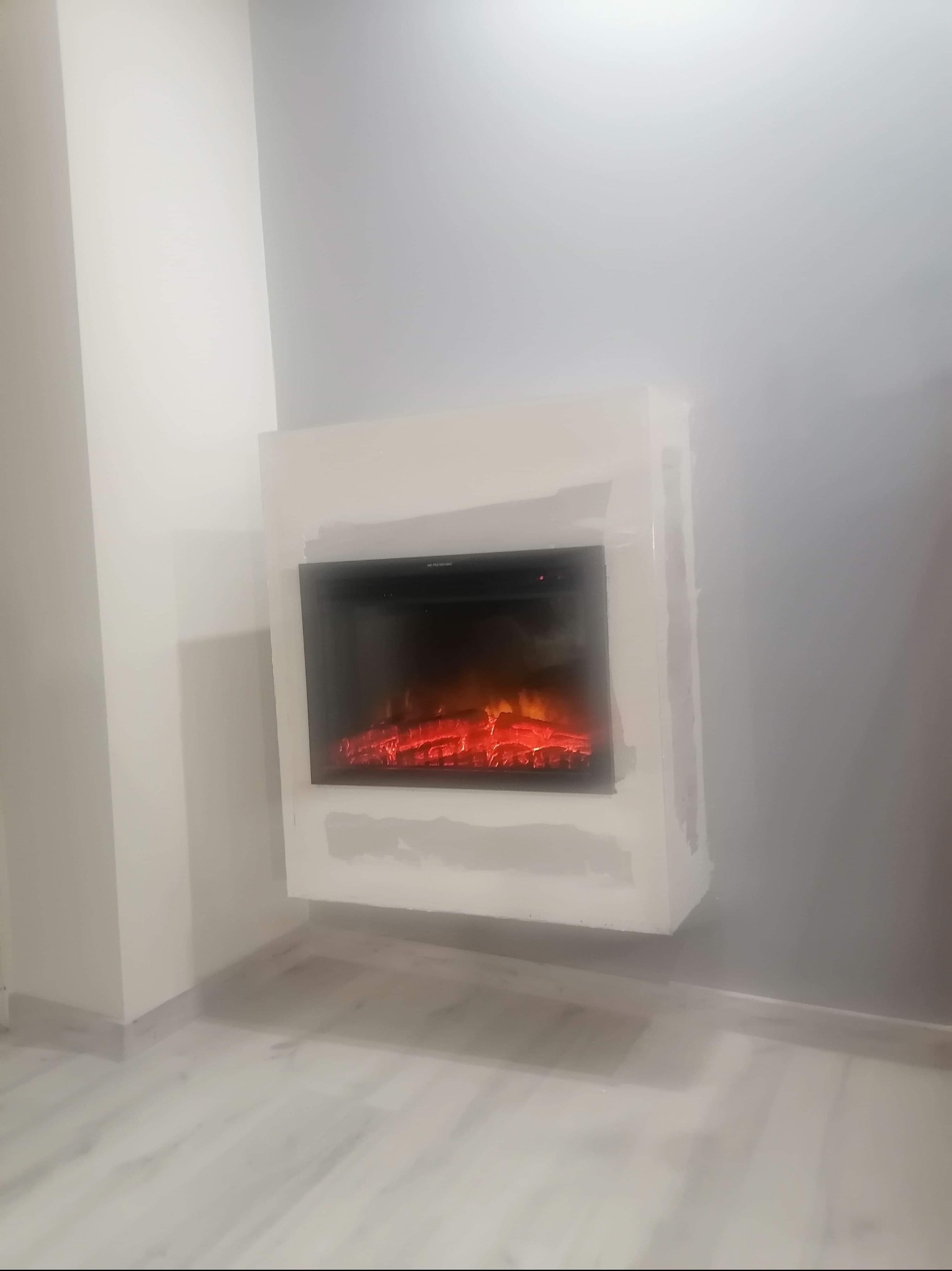 Wbudowany elektryczny kominek z obudową z płyt kartonowo-gipsowych, ślady szpachlowania widoczne na ścianie i pod kominkiem.