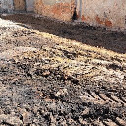 ROZBIÓRKI WYBURZENIA - Fragment zniszczonej ściany budynku z widocznymi śladami rozbiórki i gruzem na ziemi. Widoczne ślady opon ciężkiego sprzętu.