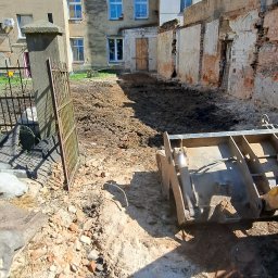 ROZBIÓRKI WYBURZENIA - Częściowo zburzony budynek z odsłoniętą cegłą, gruzem i sprzętem budowlanym w słoneczny dzień. Widoczne okna i fragmenty ścian.