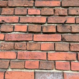 ROZBIÓRKI WYBURZENIA - Ceglana ściana z widocznym gwoździem wbitym w jedną z cegieł. Widoczne spoiny między cegłami. Fragment uszkodzonej cegły w lewym górnym rogu.