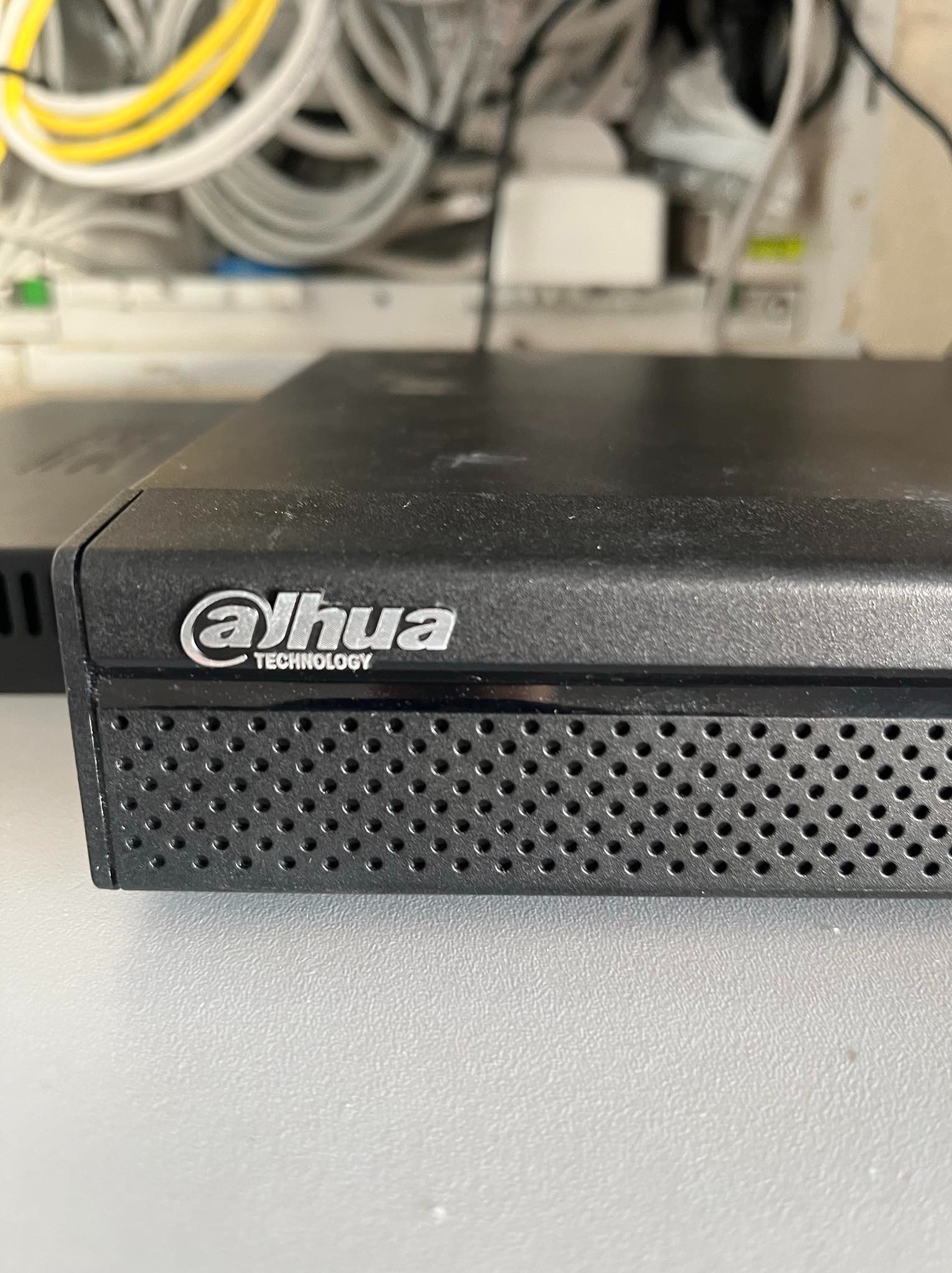 Czarny rejestrator Dahua, widoczne logo i perforowana obudowa, w tle plątanina kabli instalacyjnych.