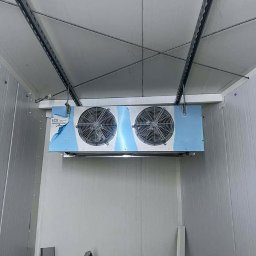 DF HYDRO TRADE SPÓŁKA Z OGRANICZONĄ ODPOWIEDZIALNOŚCIĄ - Wnętrze chłodni z zamontowanym agregatem chłodniczym ECO z dwoma wentylatorami. Widoczne metalowe profile i ściany z paneli. Częściowo zdjęta folia ochronna.