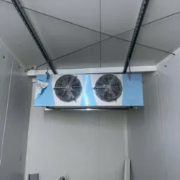 Wnętrze chłodni z zamontowanym agregatem chłodniczym ECO z dwoma wentylatorami. Widoczne metalowe profile i ściany z paneli. Częściowo zdjęta folia ochronna.