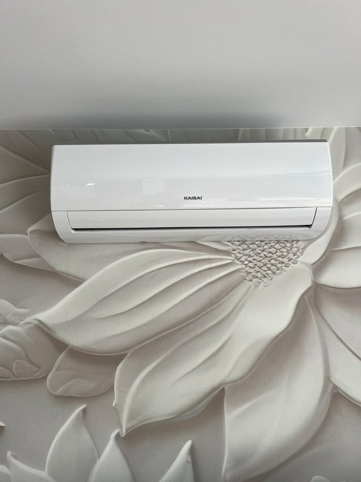 Biały klimatyzator Kaisai zamontowany na ścianie z dekoracyjną, kwiatową tapetą 3D. Nowoczesny design.