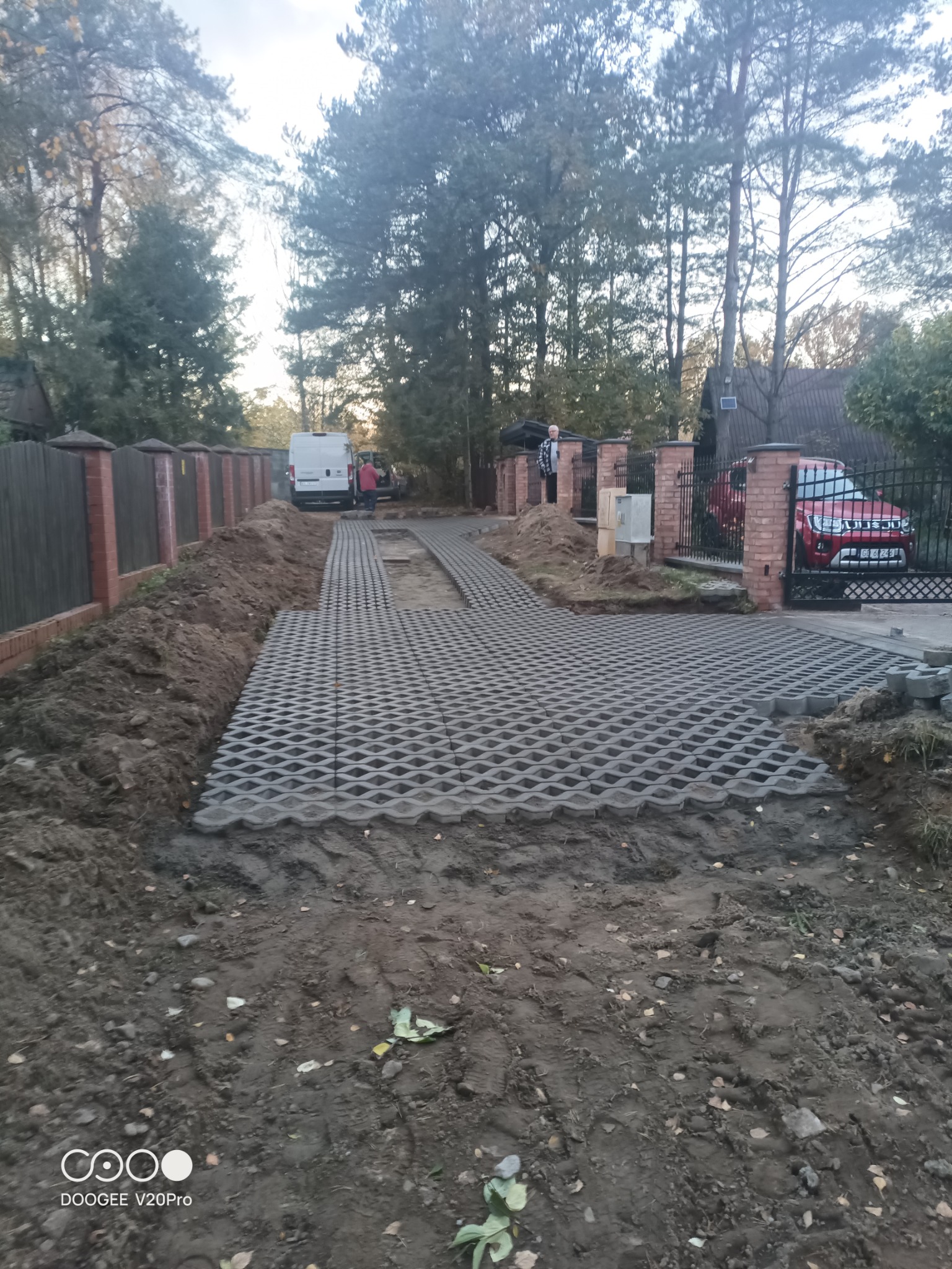 Układanie ażurowych płyt betonowych na podjeździe, widoczny częściowo ułożony fragment, przygotowane podłoże i samochody w tle.