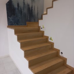 MK SCHODY Marcin Kowalczyk - Nowoczesne, dębowe schody z minimalistycznym wykończeniem, zintegrowane z białą ścianą i ozdobną tapetą z motywem leśnym, widoczne przygotowane punkty oświetleniowe.