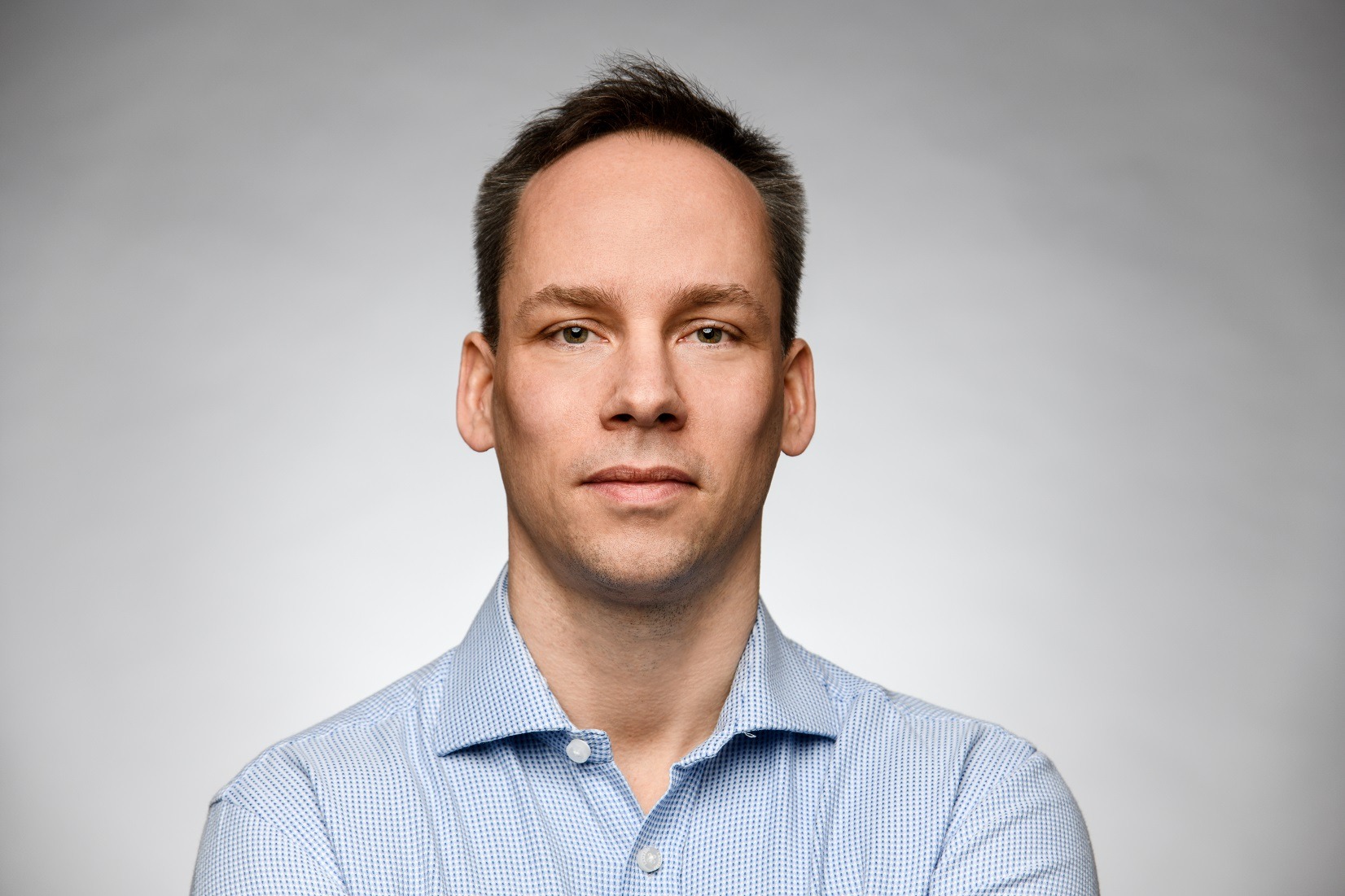 Portret biznesowy mężczyzny w Warszawie, w błękitnej koszuli z drobnym wzorem, na jasnoszarym tle.