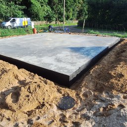 ProBudTech WOJCIECH GEMZA - Wylany fundament z izolacją pionową, otoczony piaskiem. W tle widoczny bus i zieleń. Na pierwszym planie studzienka rewizyjna.