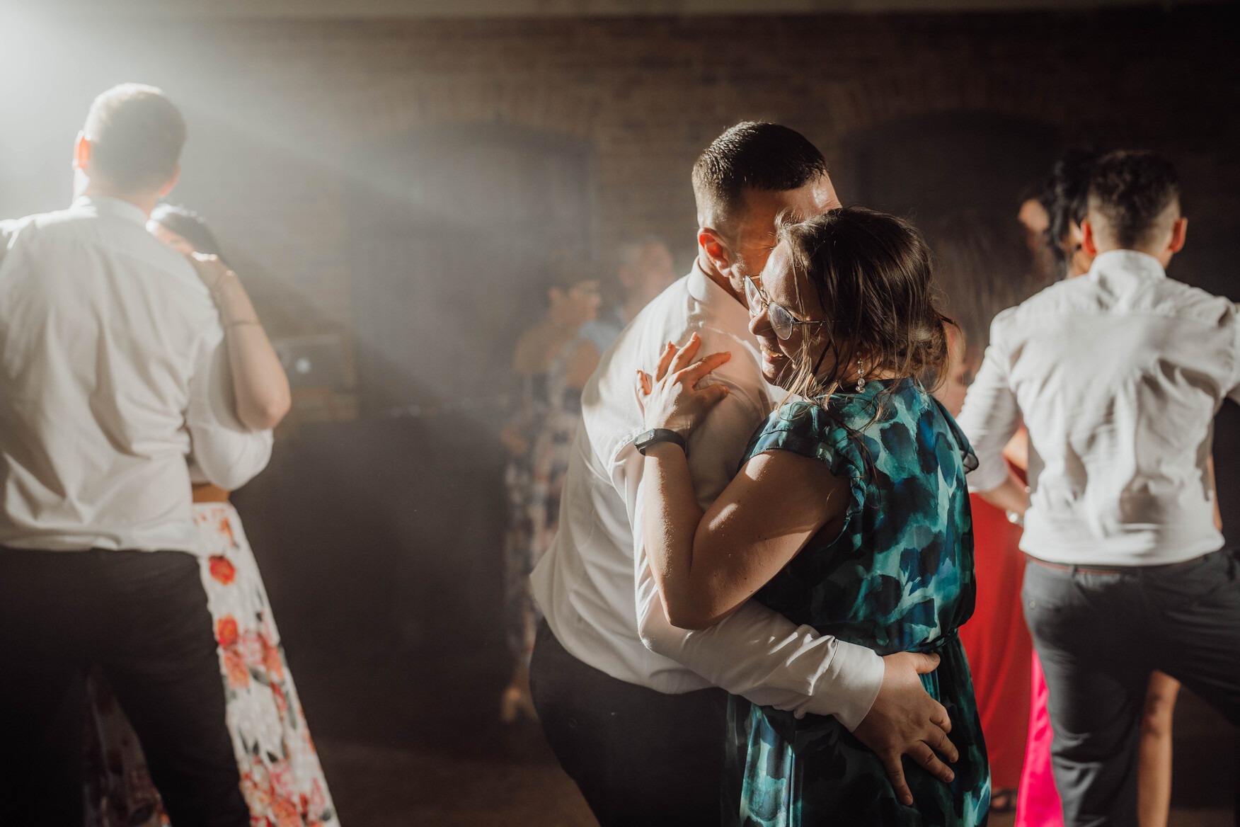 Para w objęciach tańczy podczas eventu w Pabianicach, kobieta w okularach i sukience w odcieniach zieleni, mężczyzna w białej koszuli, w tle inni goście i efekty świetlne.