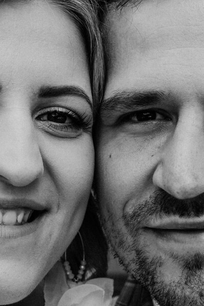 Zbliżenie na twarze uśmiechniętej pary, czarno-białe zdjęcie, widoczne detale skóry i biżuterii kobiety.