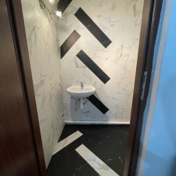 Fishka Floors Jacek Fiszka-Borzyszkowski - Mała łazienka z umywalką, biało-czarne chevrony na ścianach i podłodze, oświetlenie punktowe, widok zza uchylonych drzwi.
