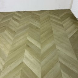 Fishka Floors Jacek Fiszka-Borzyszkowski - Jasna, drewniana podłoga ułożona we wzór jodełki, widoczne niedokończone wykończenia ścian i wystające przewody elektryczne.