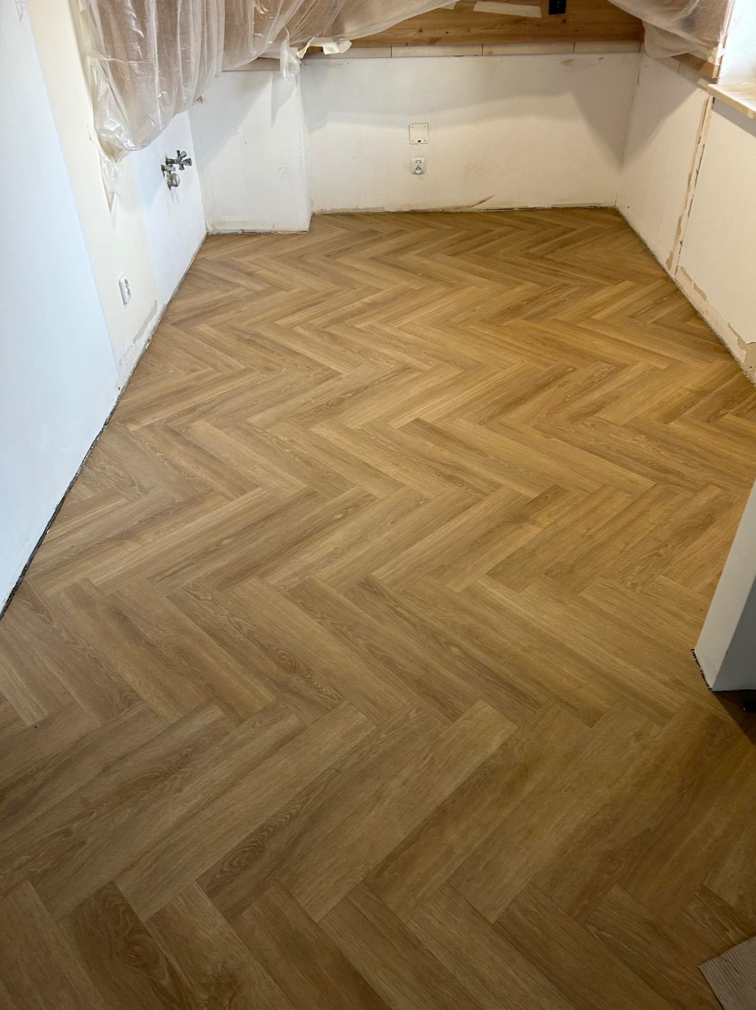 Ułożona podłoga z paneli w jodełkę w pomieszczeniu w Mielcu, ściany przygotowane do malowania, zabezpieczone folią. Widoczny fragment instalacji.