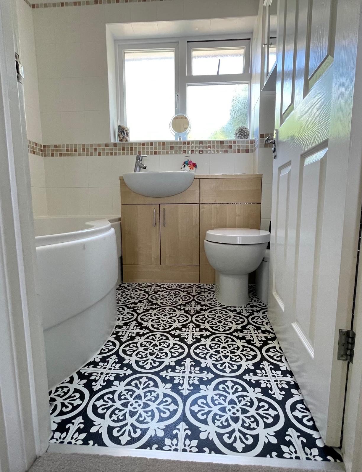 Wykończona łazienka z czarno-białą podłogą w stylu retro, jasnymi meblami pod umywalką i białą armaturą, widok zza uchylonych drzwi.