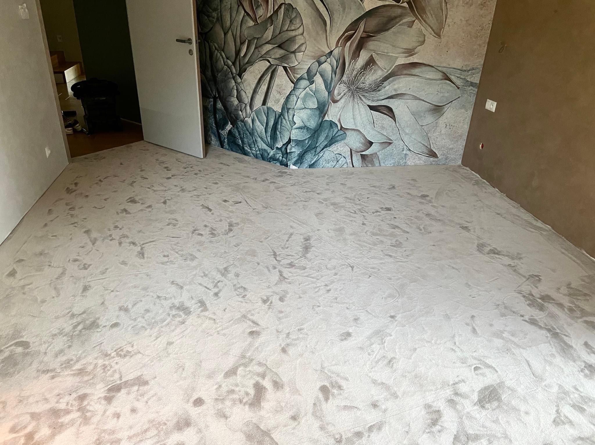 Jasnoszara podłoga w pokoju z fototapetą w kwiaty, widok z góry, otwarte drzwi do sąsiedniego pomieszczenia.