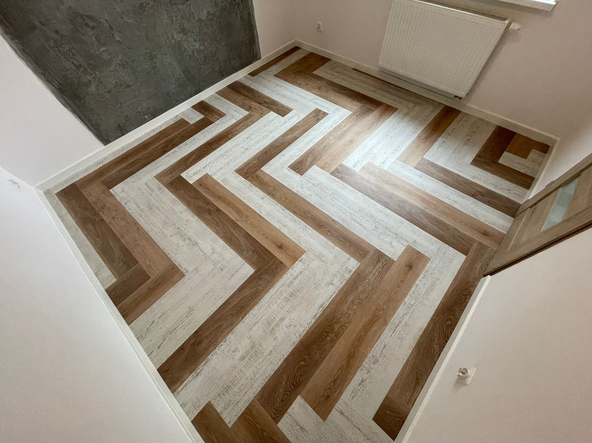 Ukończona podłoga z paneli w jodełkę, łącząca panele w odcieniach bieli i brązu, widok z góry, ściana w surowym stylu w tle.