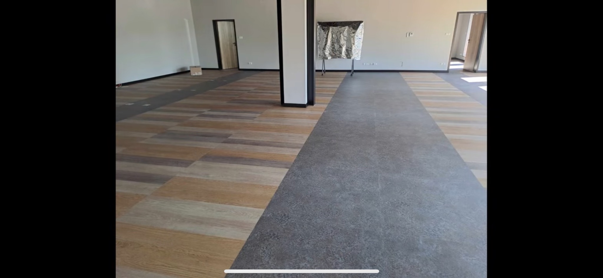 Nowoczesna podłoga w przestronnym wnętrzu, łącząca panele drewnopodobne w ciepłych odcieniach z szarymi płytkami imitującymi beton, tworząc efekt wizualnego podziału przestrzeni.