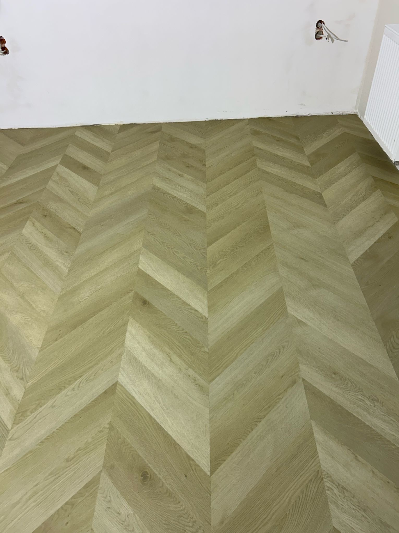 Jasna, drewniana podłoga ułożona we wzór jodełki, widoczne niedokończone wykończenia ścian i wystające przewody elektryczne.