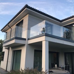 Prestiz Loft - Nowoczesny dom z balkonami zabezpieczonymi szklanymi balustradami, widok z dołu, błękitne niebo w tle. Minimalistyczny design.