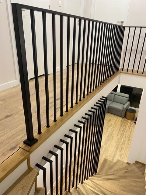 Nowoczesna, czarna balustrada z pionowych prętów na drewnianych schodach i antresoli, widok z góry, jasne wnętrze.