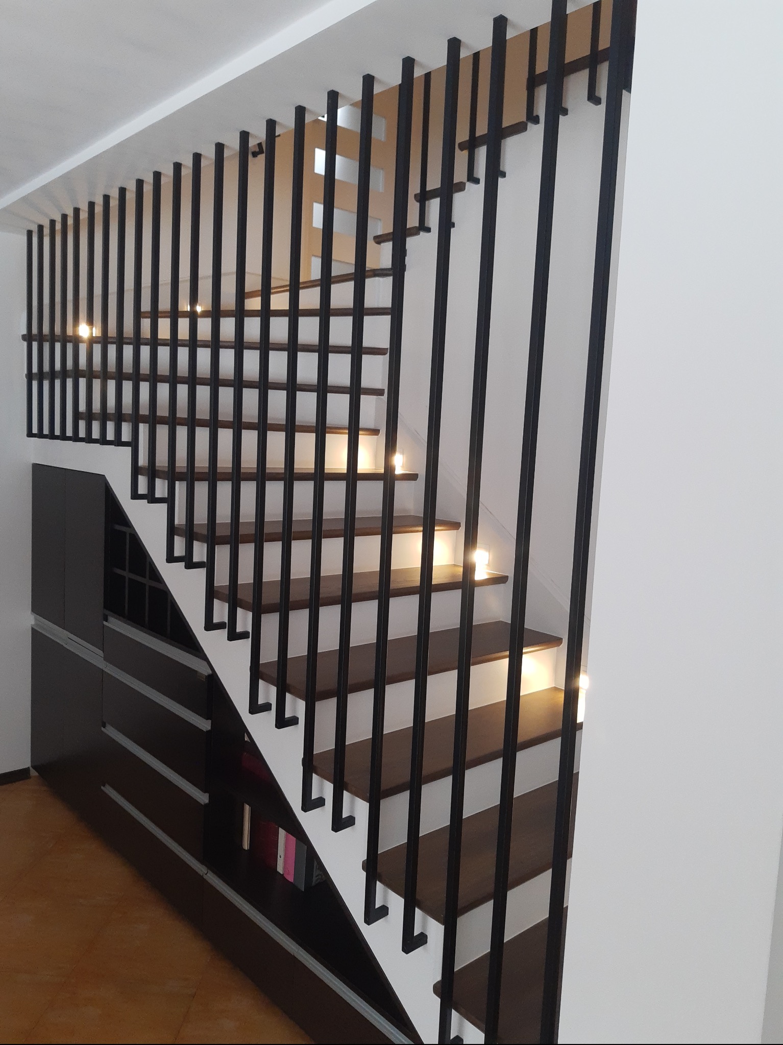 Nowoczesne schody z drewnianymi stopniami i czarną, metalową konstrukcją w Warszawie. Minimalistyczny design z oświetleniem punktowym na każdym stopniu.