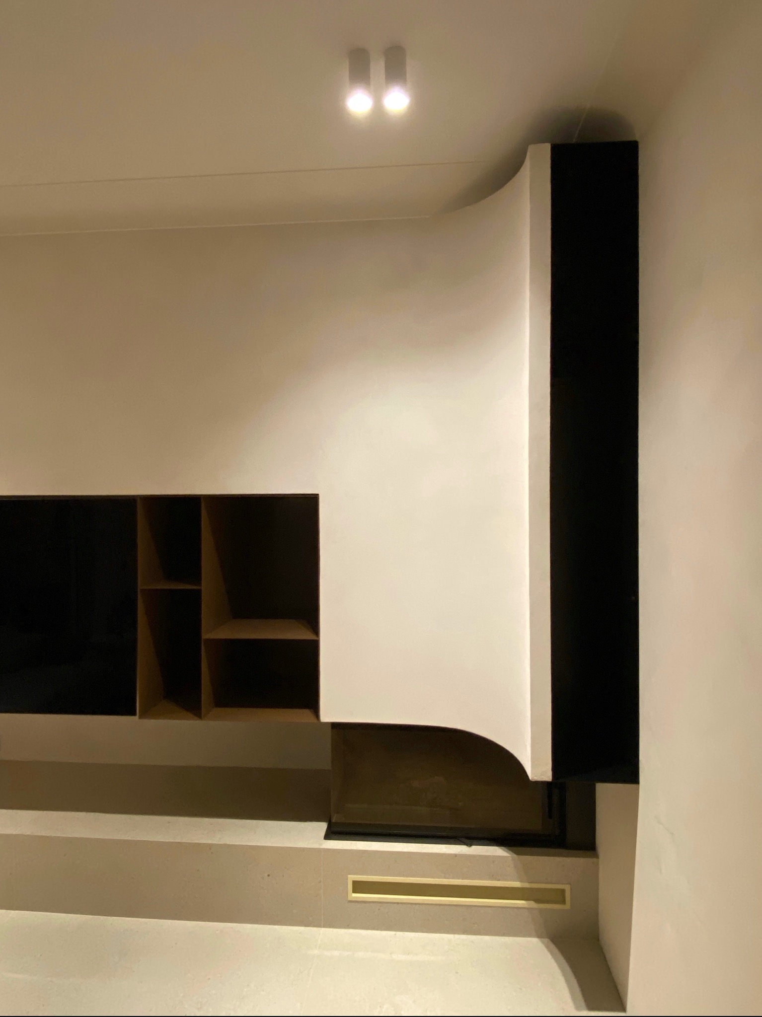 Nowoczesna zabudowa kominkowa z półkami i czarnym elementem dekoracyjnym, oświetlona punktowo, w minimalistycznym wnętrzu. Ujęcie z bliska, podkreślające detale wykończenia.