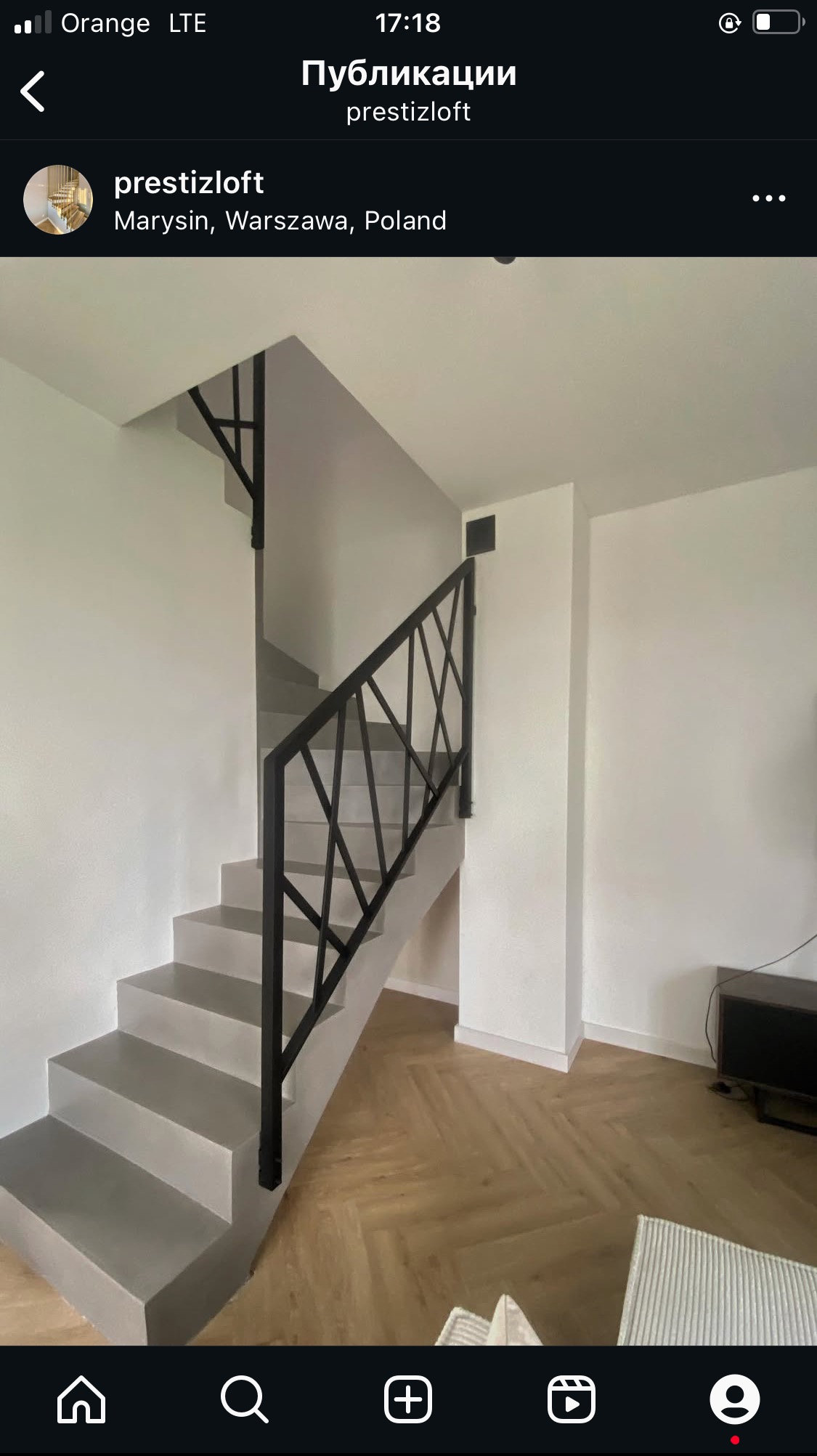 Nowoczesne schody z szarą betonową konstrukcją i czarną, geometryczną poręczą. Parkiet w jodełkę na podłodze. Minimalistyczny design w jasnym wnętrzu.