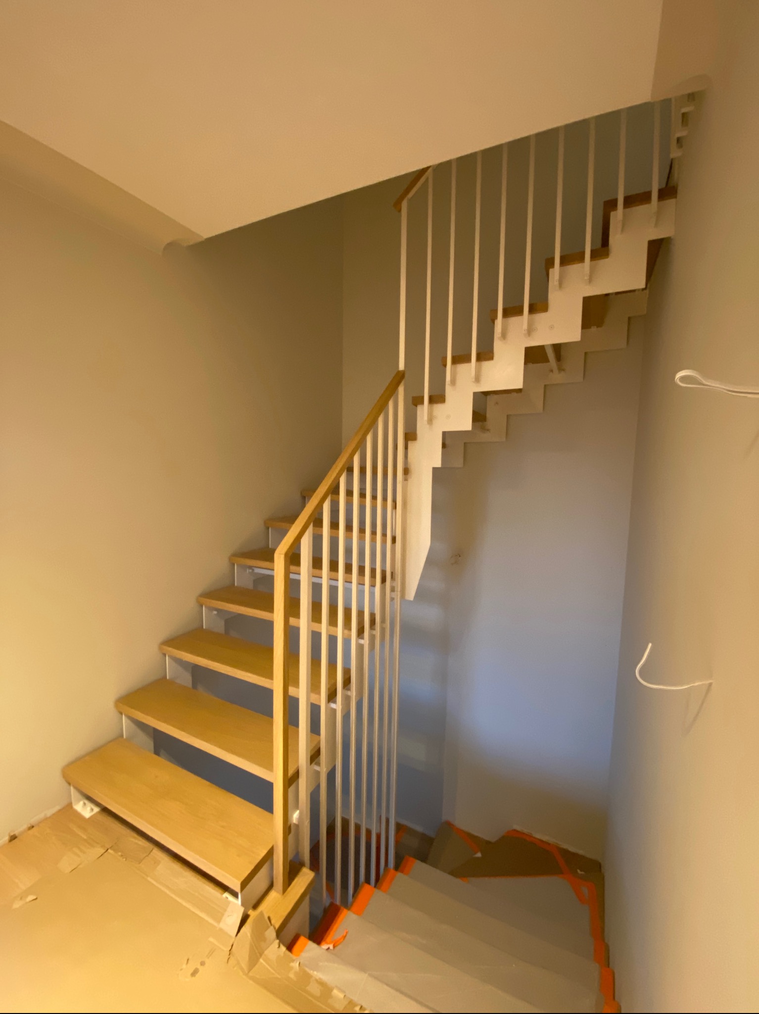 Jasne drewniane schody z białymi, pionowymi balustradami w nowoczesnym wnętrzu. Widok z dołu, z zabezpieczeniem podłogi kartonem.