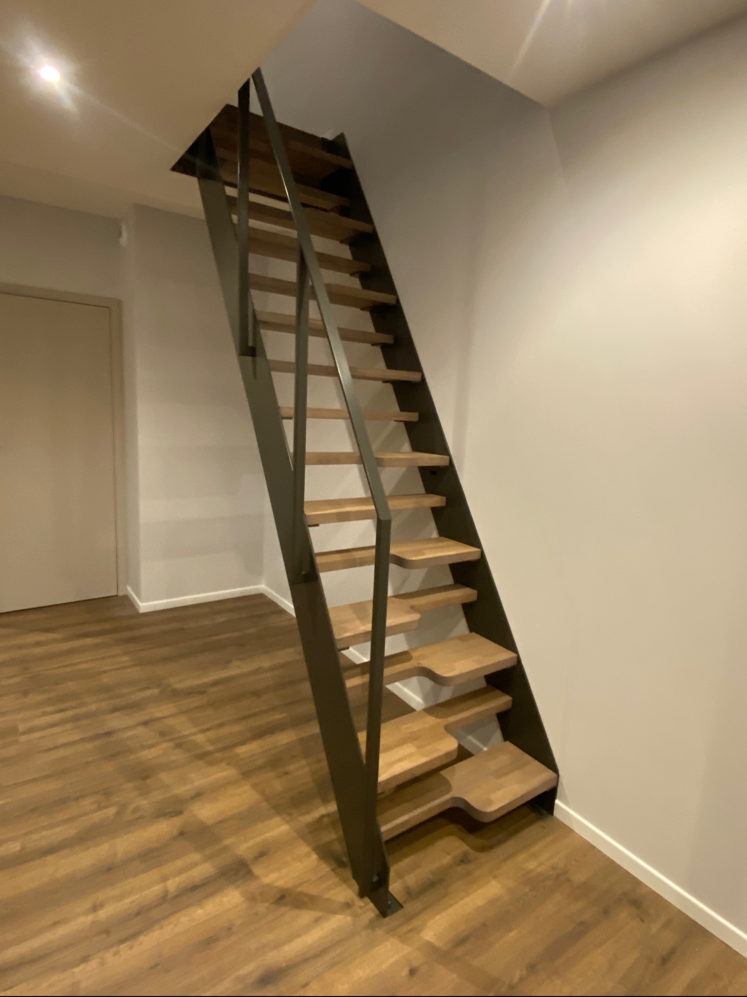 Nowoczesne schody metalowe z drewnianymi stopniami, minimalistyczny design, widok z dołu, jasne wnętrze, drewniana podłoga, oświetlenie punktowe.