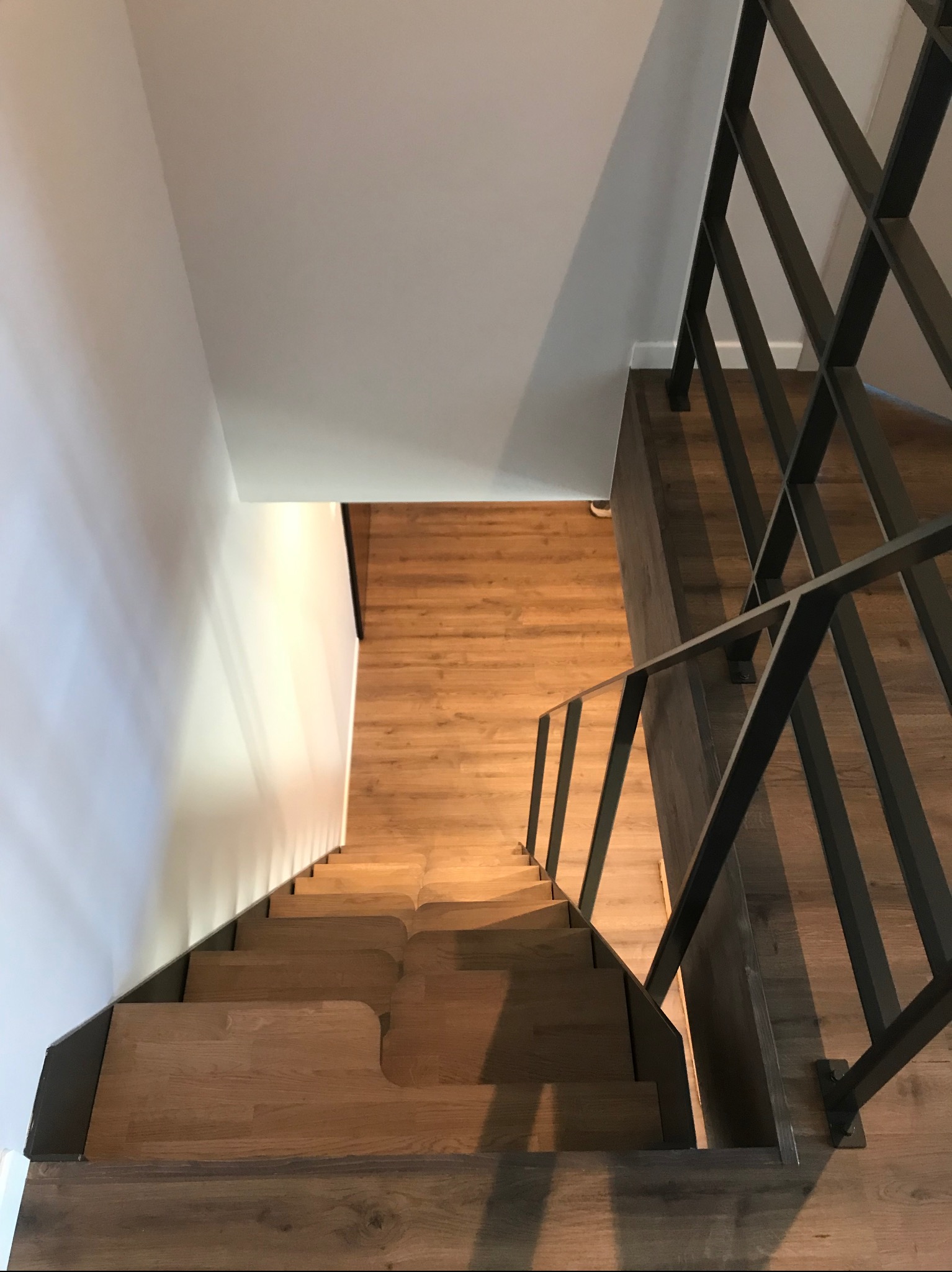 Nowoczesne schody drewniane z metalową balustradą, widok z góry. Minimalistyczny design, jasne drewno stopni kontrastuje z ciemną, geometryczną konstrukcją balustrady.