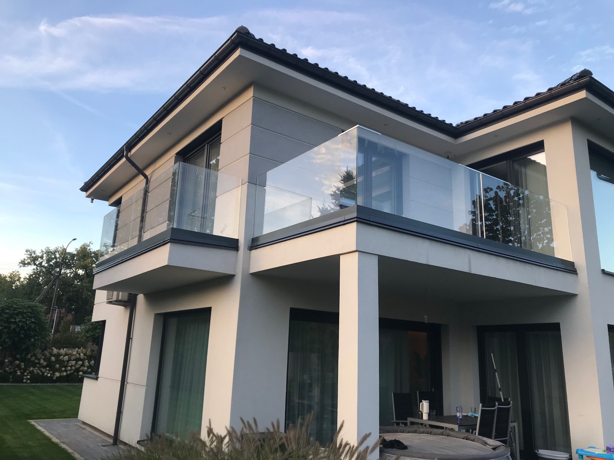 Nowoczesny dom z balkonami zabezpieczonymi szklanymi balustradami, widok z dołu, błękitne niebo w tle. Minimalistyczny design.