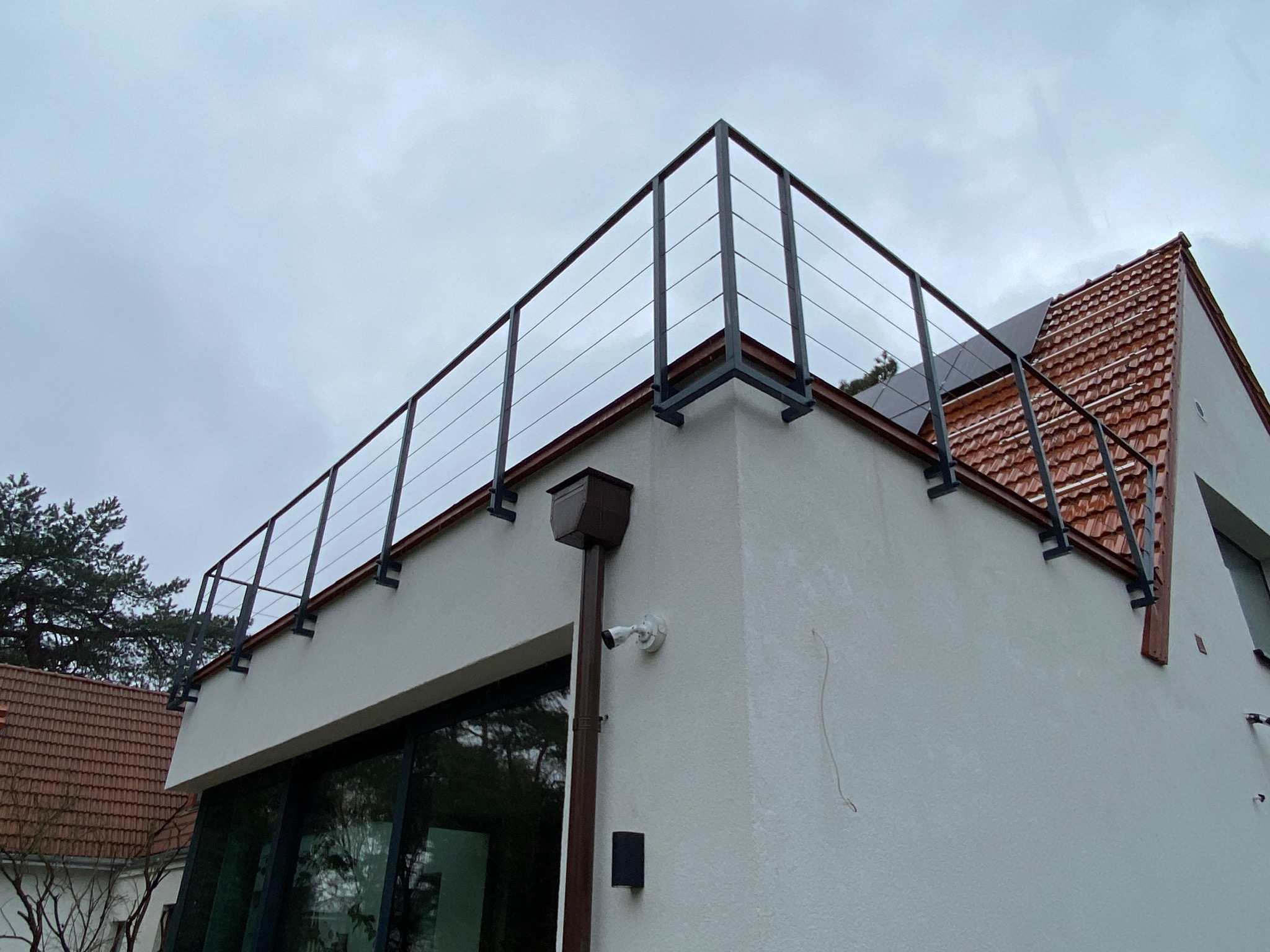 Nowoczesna balustrada ze stali nierdzewnej z linkami na tarasie domu jednorodzinnego. Widok z dołu, pochmurne niebo w tle.