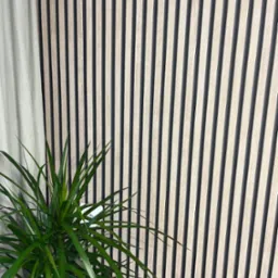 Panel ścienny z drewnianych listew w Wieliczce, z widoczną zieloną rośliną doniczkową i fragmentem zasłony.